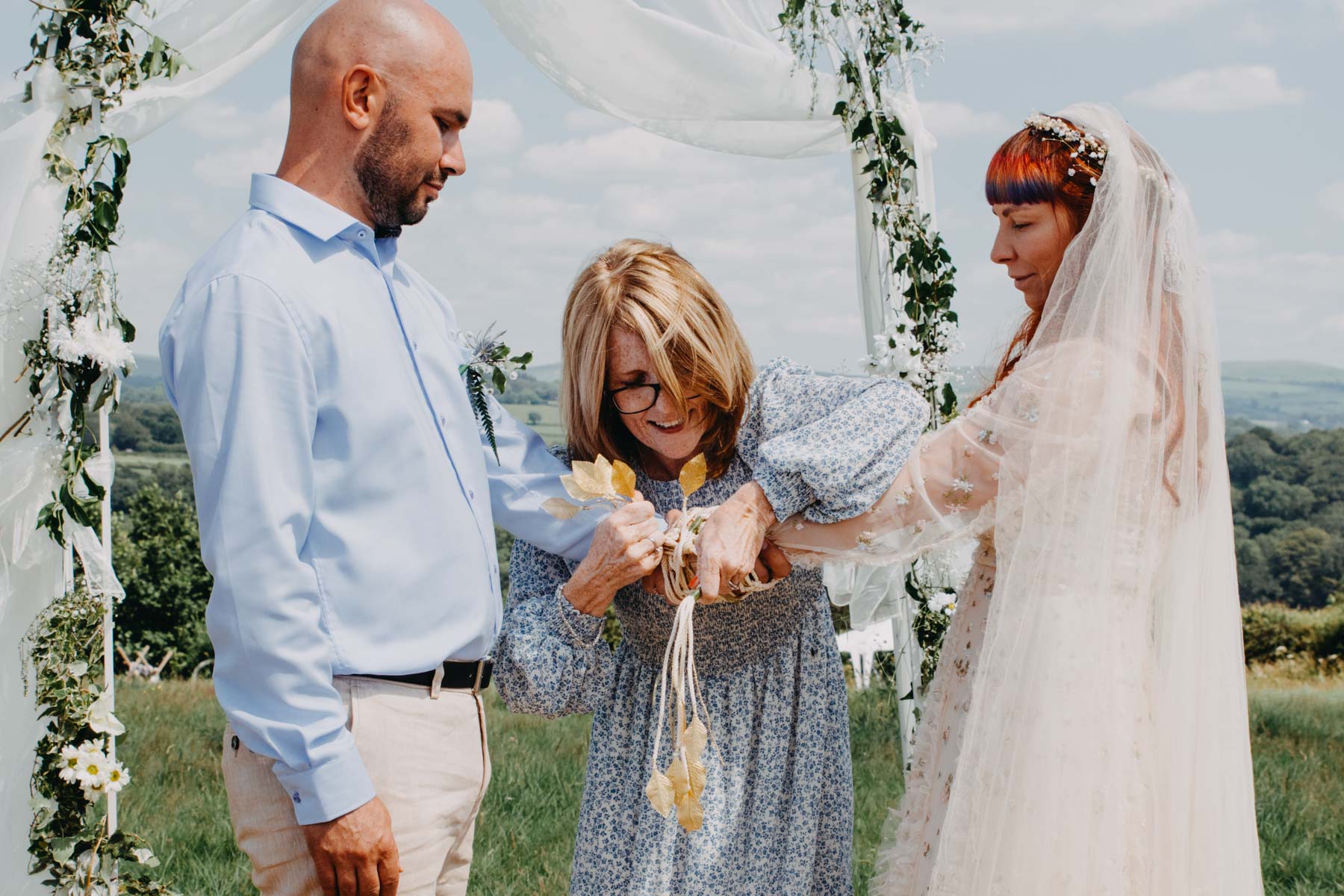 Bride and groom and celebrant binding the ribbon during the handfasting ceremony