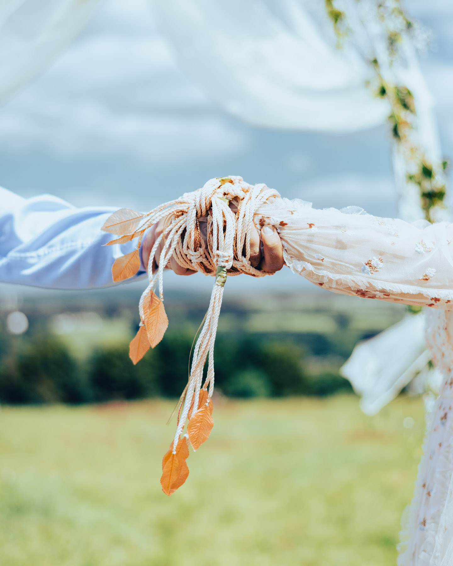 Handfasting ceremony - hands tied with a ribbon against the background of the sky and meadows