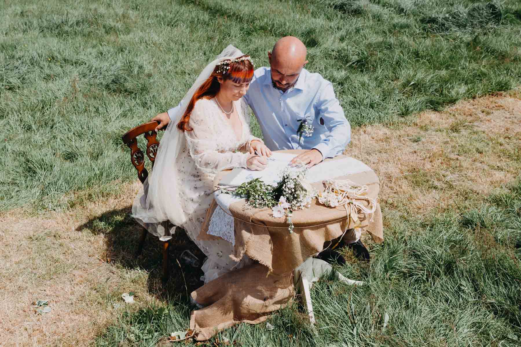 The bride and groom sign documents lying on a table standing in a meadow