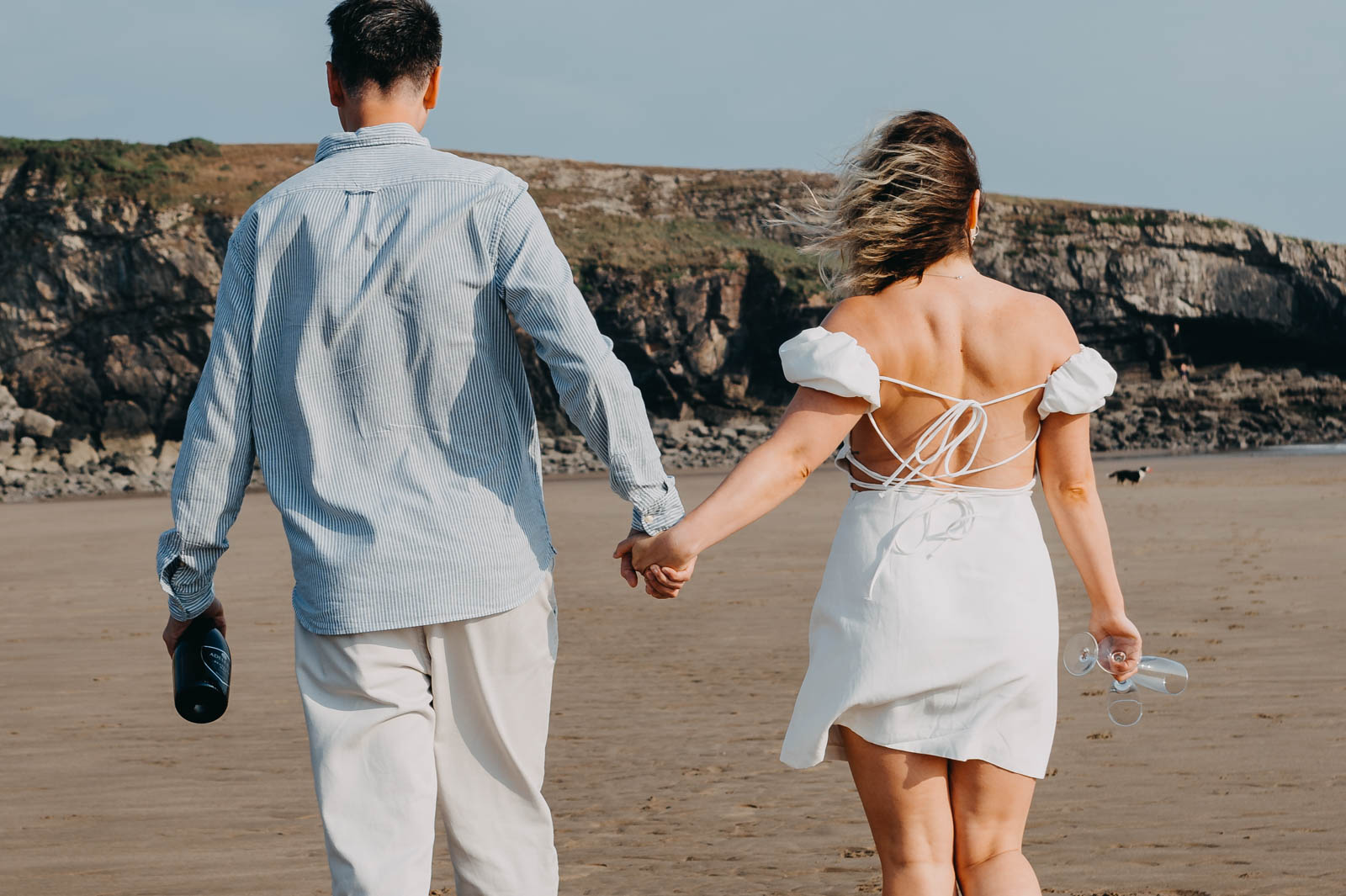 Engaged couple walks ahead on the beach during the engagement photoshoot Wales.