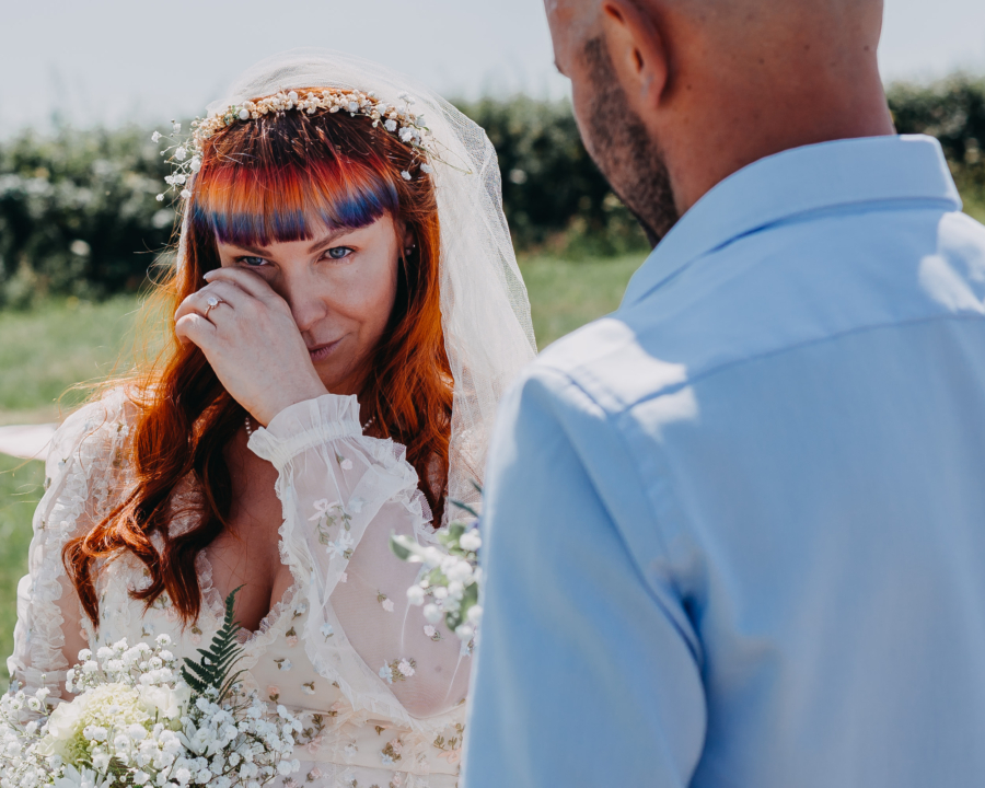 A bride wiping away tears during an outdoor ceremony, captured in a candid and emotional moment.
