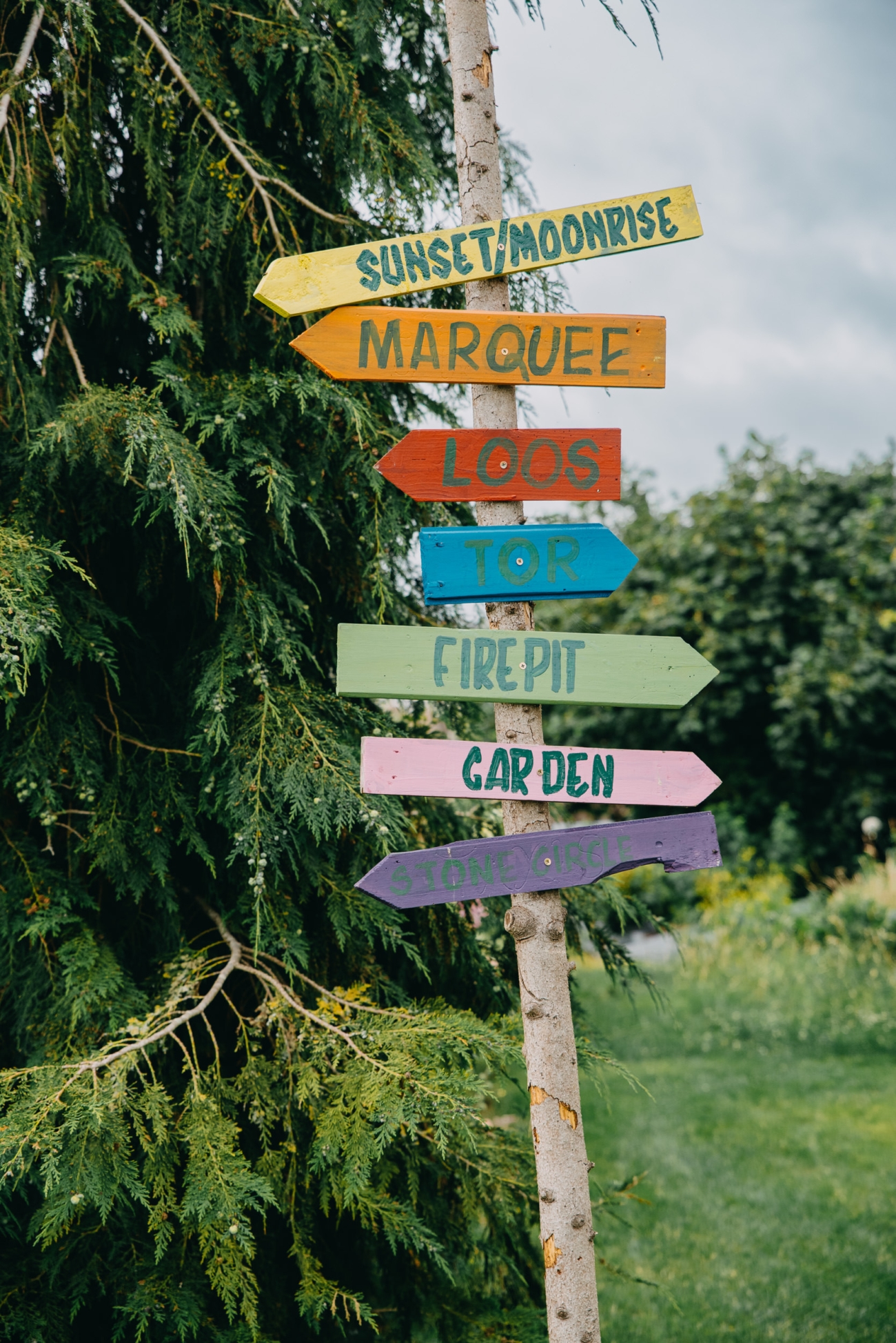 Colourful directional sign at Splotts Moor in Glastonbury, pointing to various locations like the marquee, firepit, and garden.
