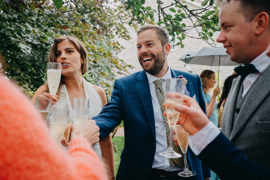 A candid wedding photography moment capturing the bride and groom toasting with champagne during an outdoor celebration.