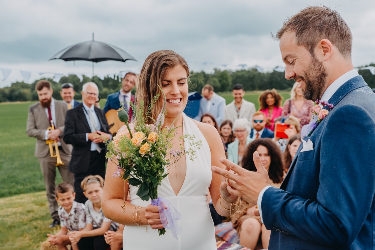 The bride places the wedding ring on the groom's finger during an outdoor ceremony.