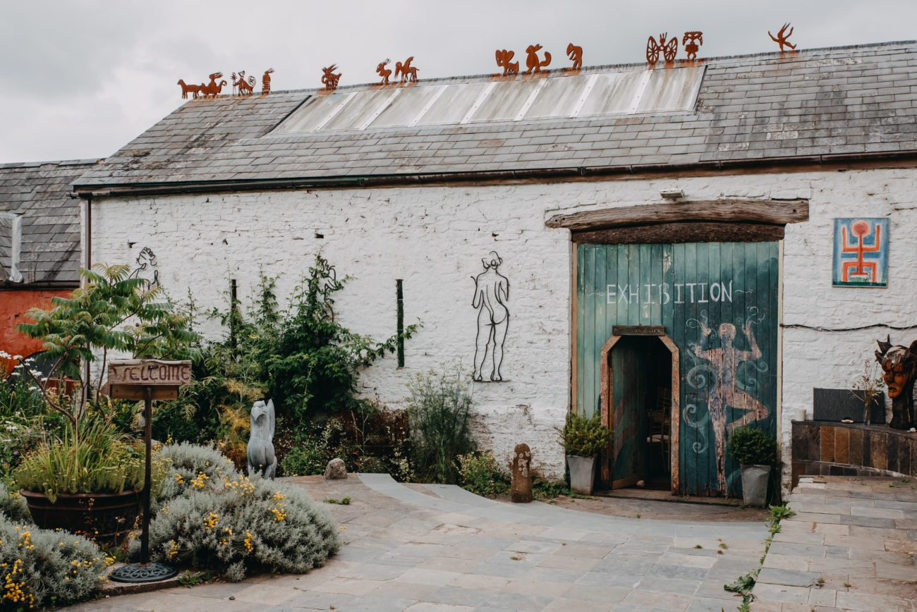 Artistic exhibition space at Coed Weddings venue near Cowbridge, Wales, featuring rustic decor with quirky metal sculptures on the roof and hand-drawn artwork on the walls.