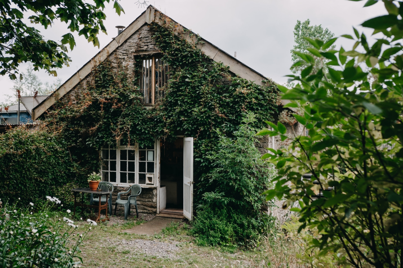 Charming ivy-covered cottage at Coed Weddings in Cowbridge, Wales, featuring a rustic outdoor seating area surrounded by lush greenery.