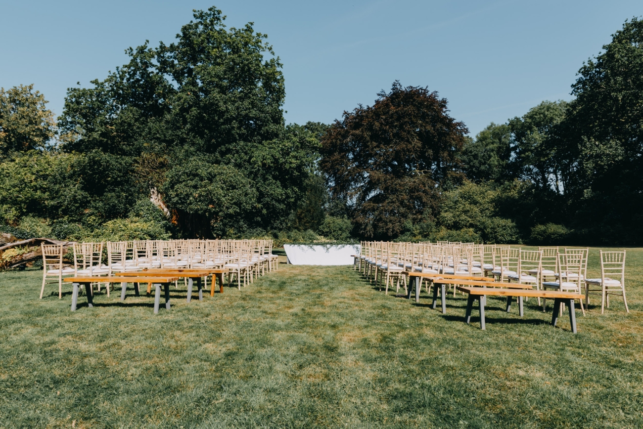 Outdoor wedding ceremony setup at Glansevin Mansion, Brecon Beacons, with rows of wooden chairs on the manicured lawn, framed by lush greenery and mature trees, offering a serene and picturesque setting.