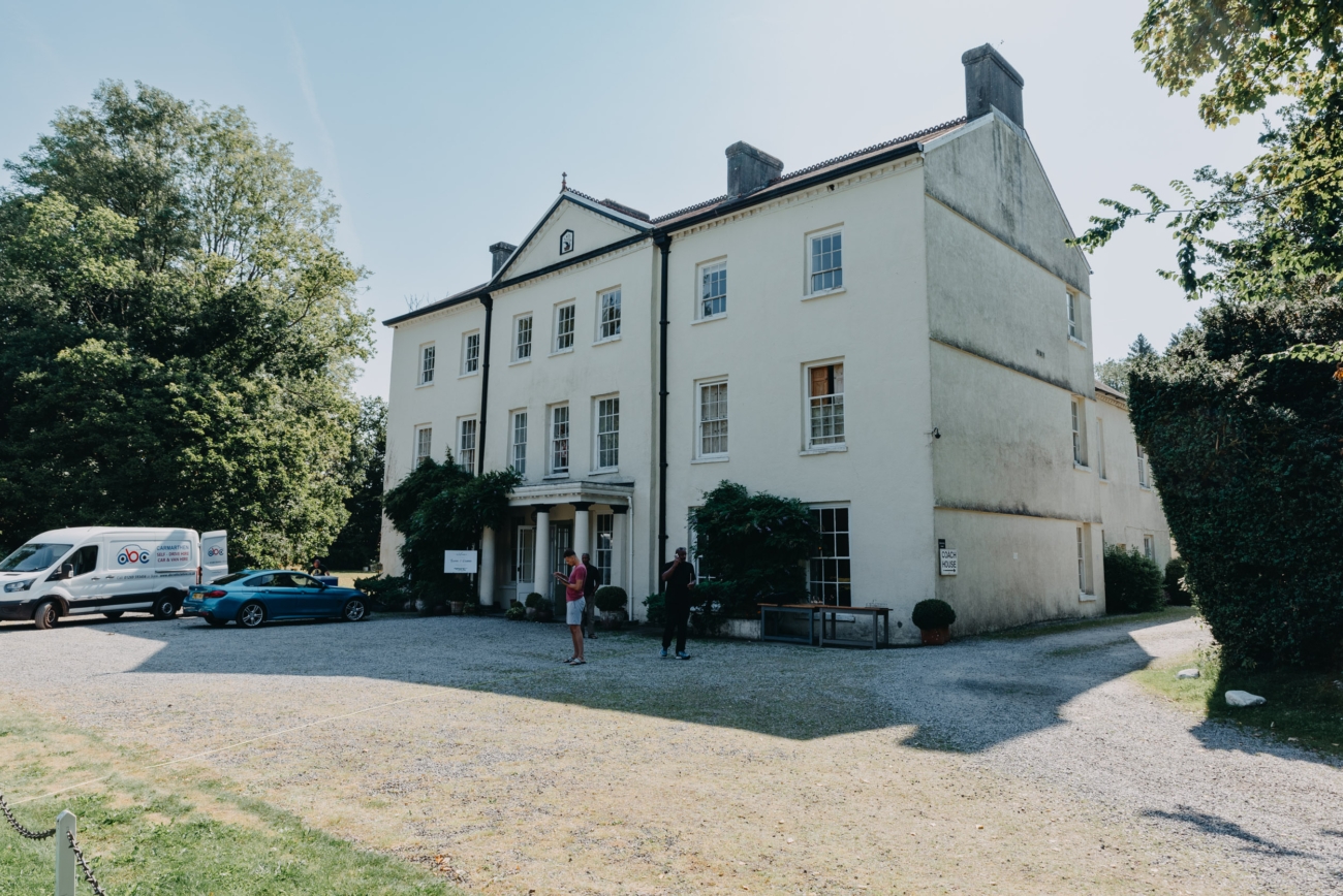 Front view of Glansevin Mansion in Llangadog, a grand Georgian building with a classic facade, surrounded by trees and a gravel driveway, providing an elegant setting for weddings and events.