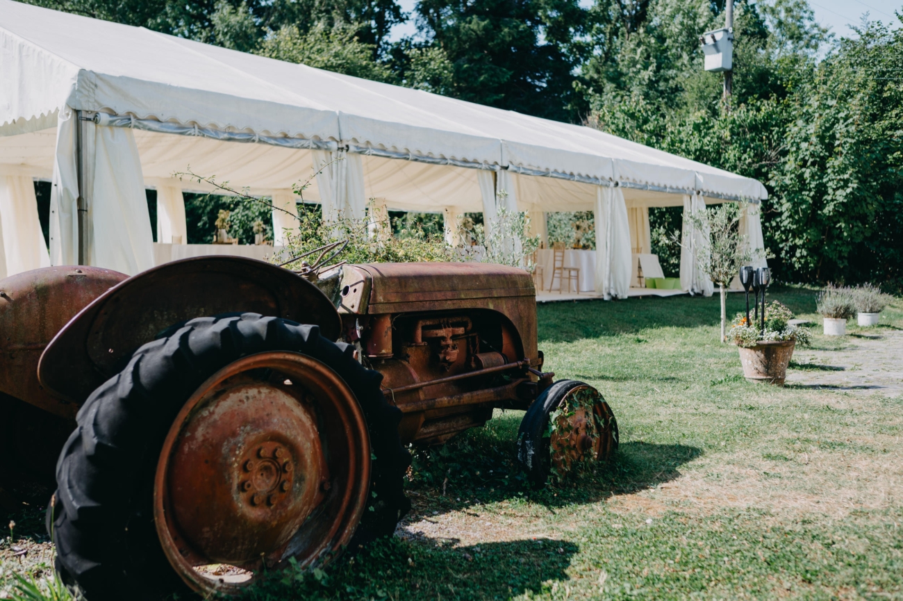 A vintage rusted tractor sits in the foreground of a lush green lawn, with a white marquee tent in the background at Glansevin Mansion, Llangadog, creating a charming rustic wedding scene.