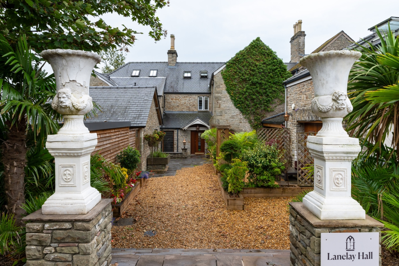 Entrance to Lanelay Hall, a historic wedding venue in Pontyclun, featuring stone pillars and a charming courtyard with greenery and flowers.