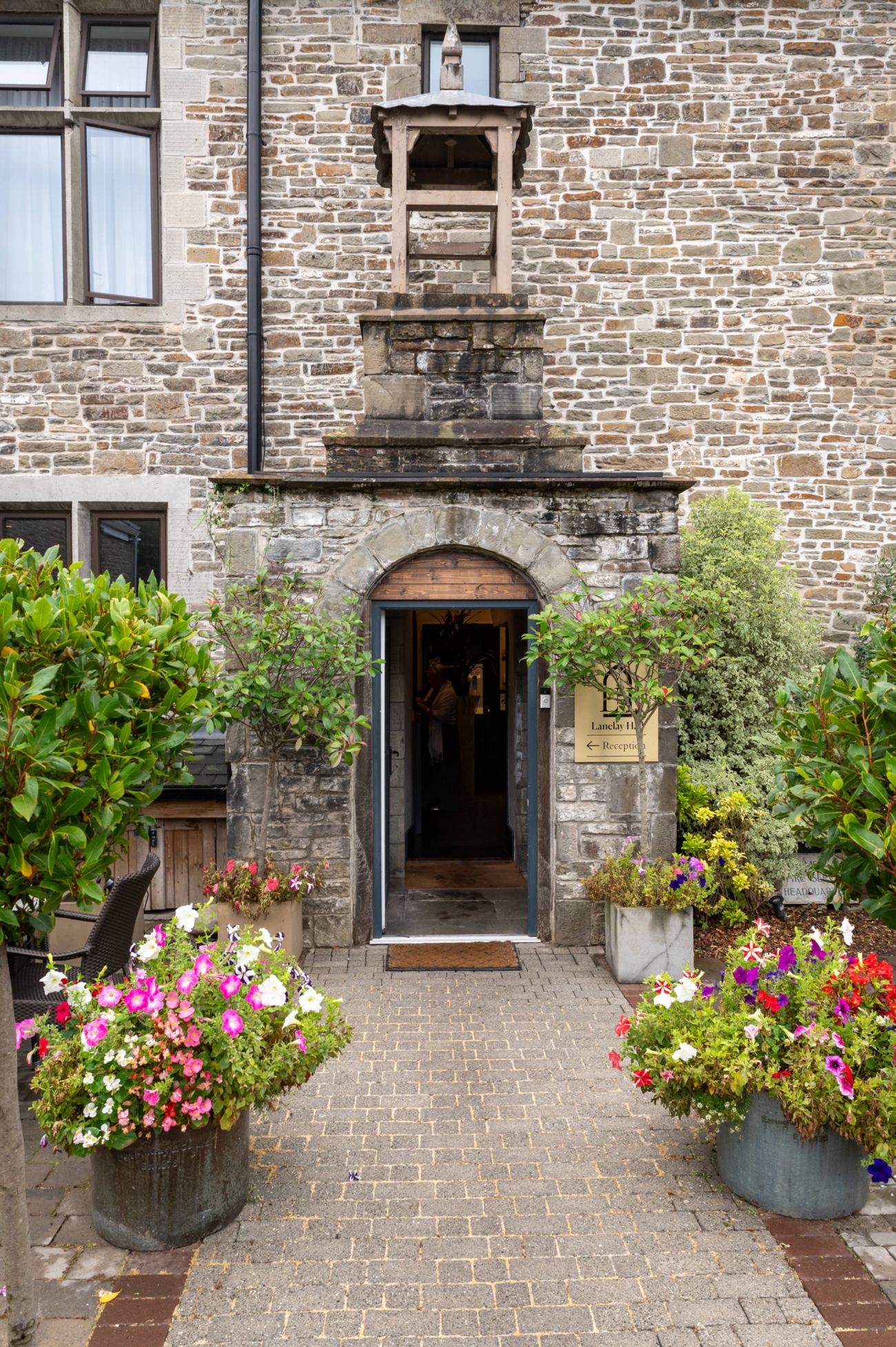 Historic stone entrance of Lanelay Hall in Pontyclun, a luxury wedding venue, with vibrant flower pots and elegant archway leading to the reception area.