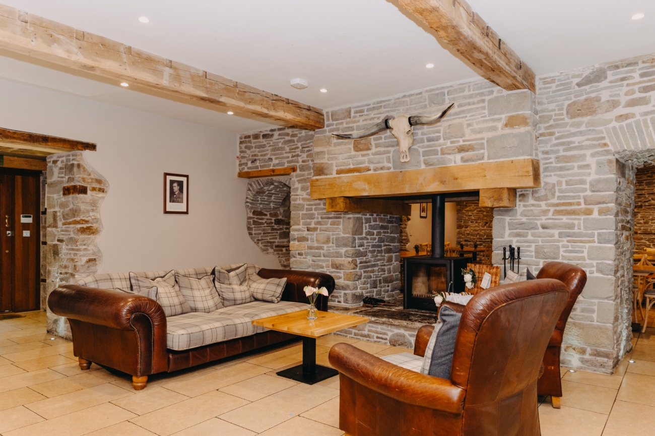 Rustic lounge area at Lanelay Hall in Pontyclun, featuring leather sofas, a stone fireplace with a mounted skull, and exposed wooden beams, creating a cosy and welcoming atmosphere for wedding guests.