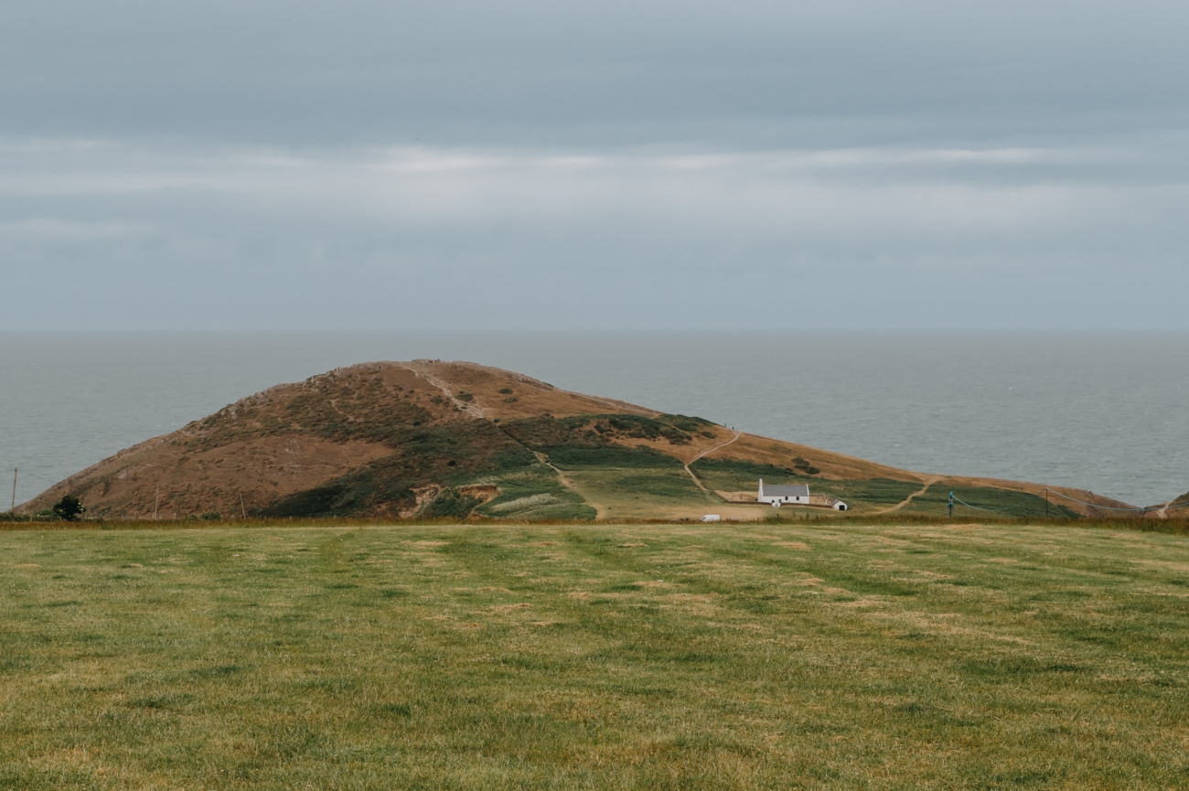 A breathtaking view of the Mwnt coastline, showcasing the rugged hills and the iconic white church of Mwnt near The Shed, a unique wedding venue in Wales.