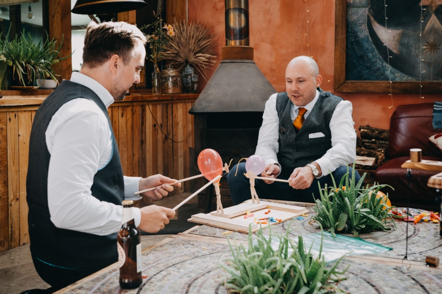 Groom and best man enjoying a fun balloon game during a wedding reception, captured by a candid wedding photographer.