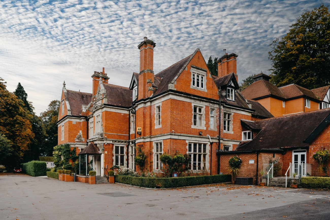 Front view of the historic Coed-Y-Mwstwr Hotel near Bridgend, featuring red brick architecture and a grand entrance, ideal for a charming wedding venue.