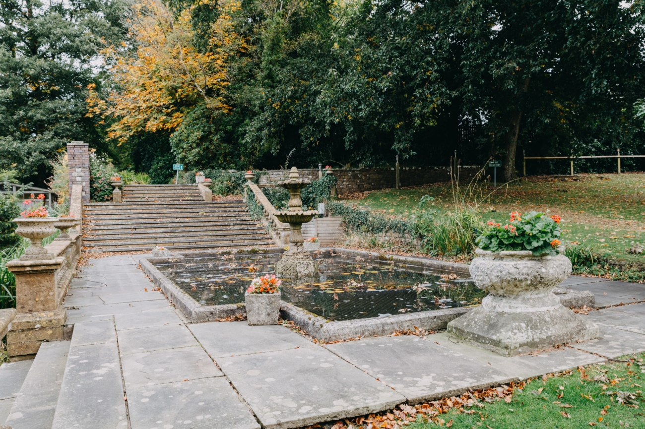 A beautiful stone fountain surrounded by vibrant flowers and a grand staircase in the gardens of Court Colman Manor, a picturesque wedding venue near Bridgend.