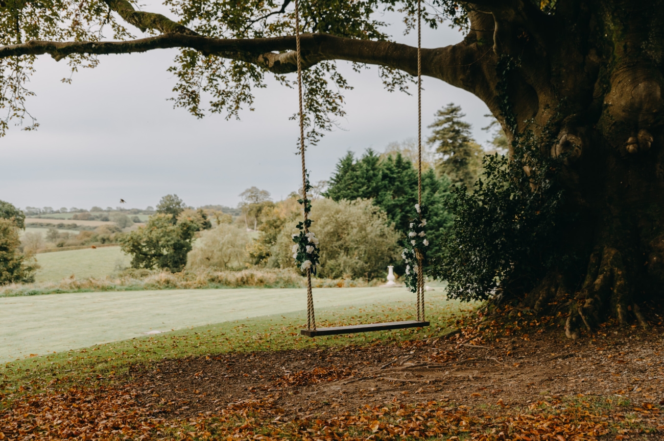 A picturesque tree swing adorned with floral decorations, overlooking the rolling countryside at Court Colman Manor, a romantic wedding venue near Bridgend.