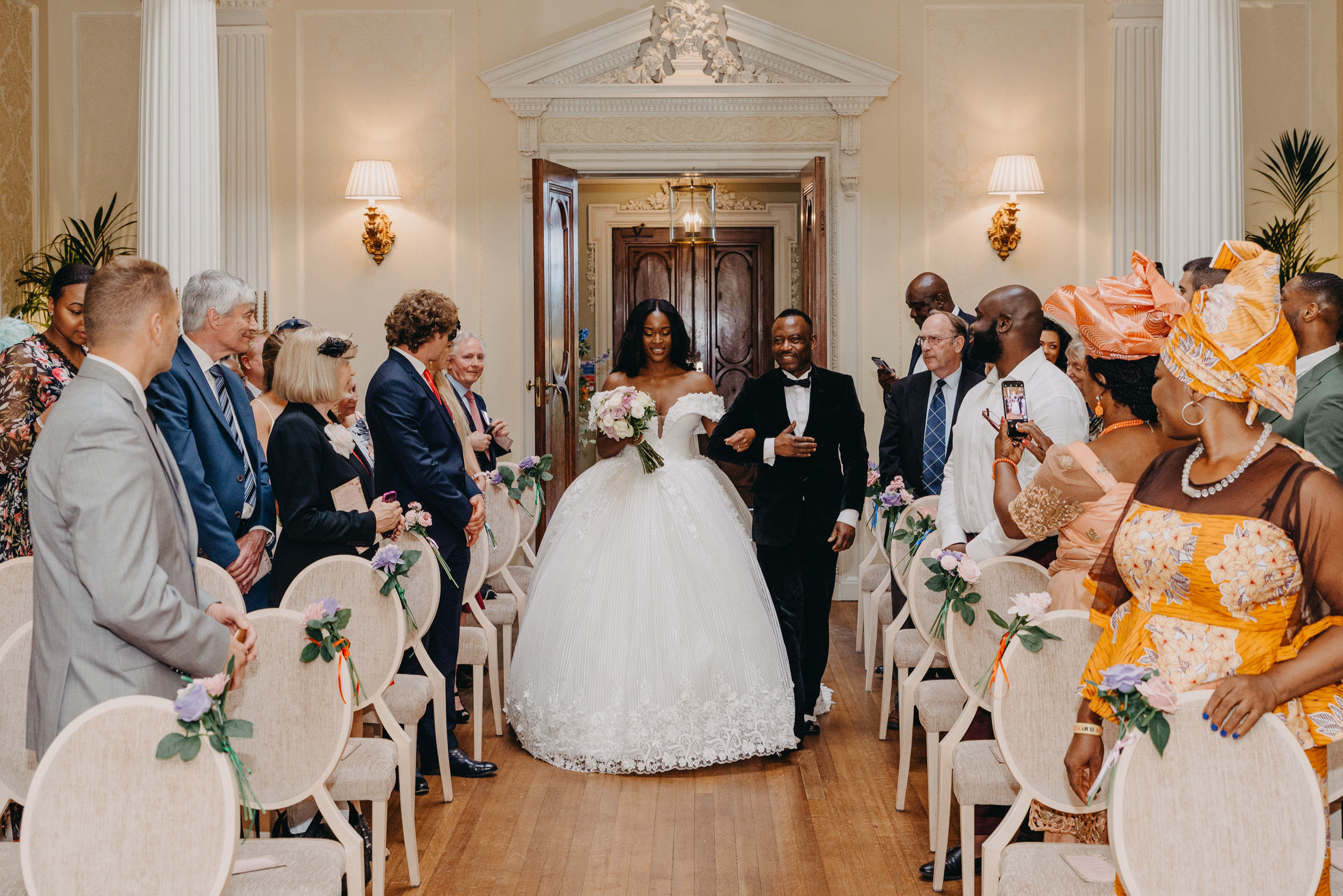 Bride walking down the aisle with her father surrounded by family and friends - documentary style wedding photography.