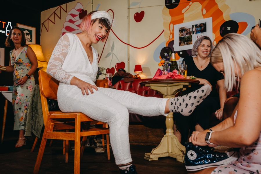 Bride laughing while getting ready, wearing fun heart-patterned socks, captured candidly during an authentic wedding moment in a relaxed setting.