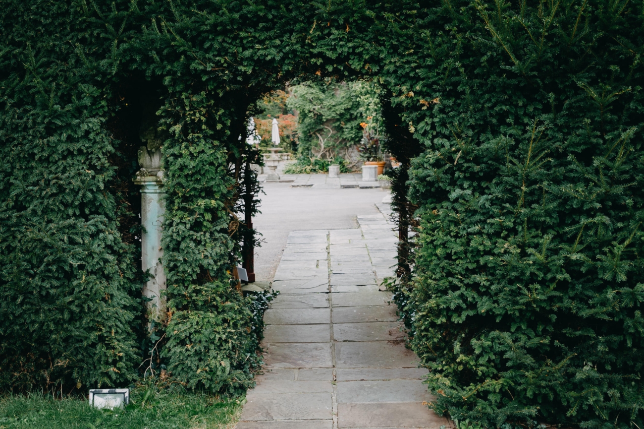 A charming stone pathway framed by an archway of lush greenery at Miskin Manor, leading into a peaceful garden courtyard.