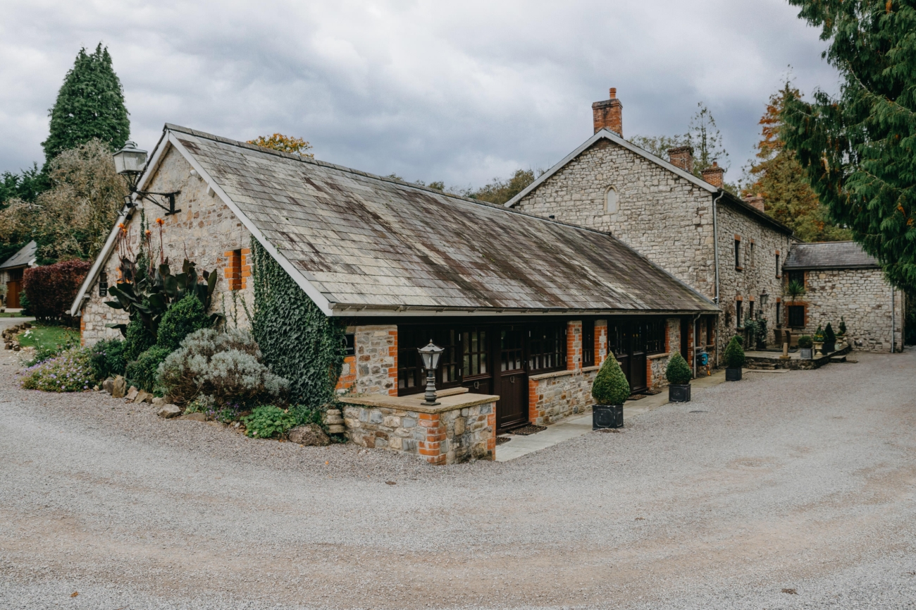 Historic stone building at Pencoed House Estate, surrounded by greenery and well-manicured shrubs, offering a charming and rustic atmosphere for weddings and events in South Wales.