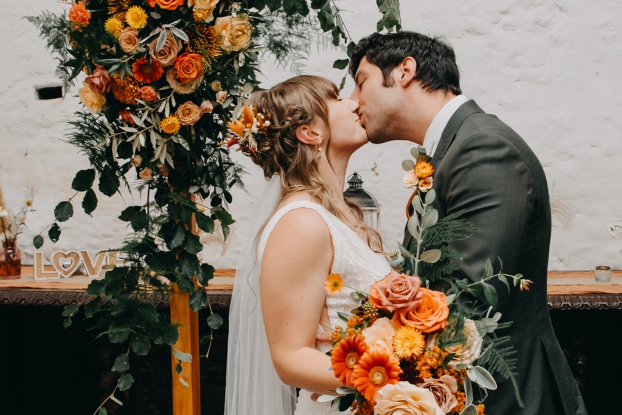Bride and groom sharing a romantic kiss under a floral arch, celebrating their love and the success of finding a reliable wedding photographer to capture these special moments.
