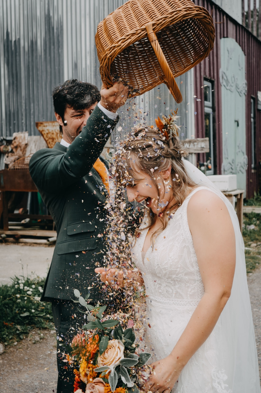 Groom playfully pouring a basket of confetti over the laughing bride, capturing a joyful and spontaneous wedding moment, taken by a candid wedding photographer.