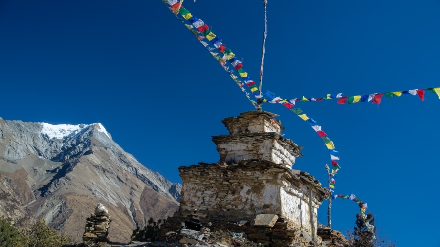 Ancient stone stupa with Tibetan prayer flags on the Annapurna Circuit with a snow-capped peak in the background.