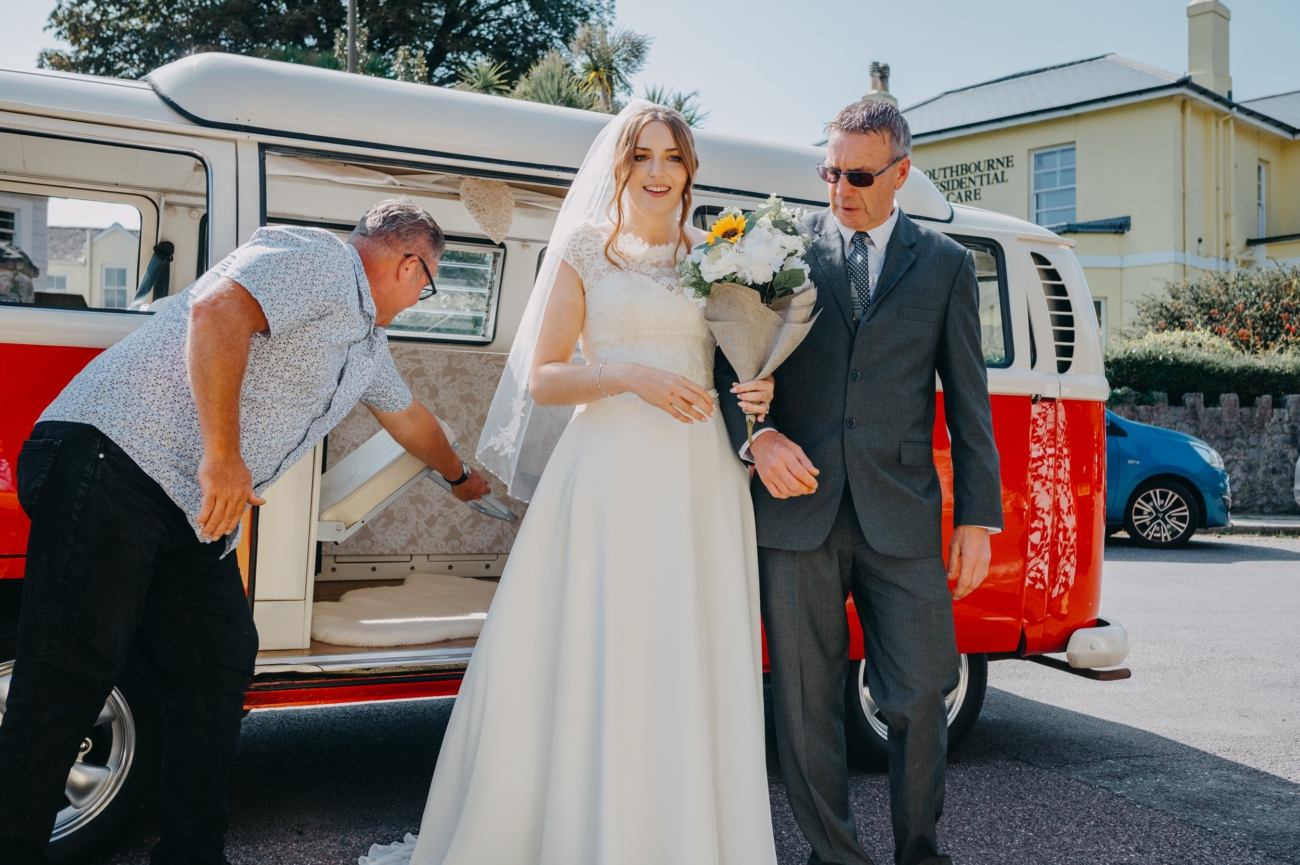 Bride arrives at All Saints Church Babbacombe in a classic red VW campervan, escorted by her father.
