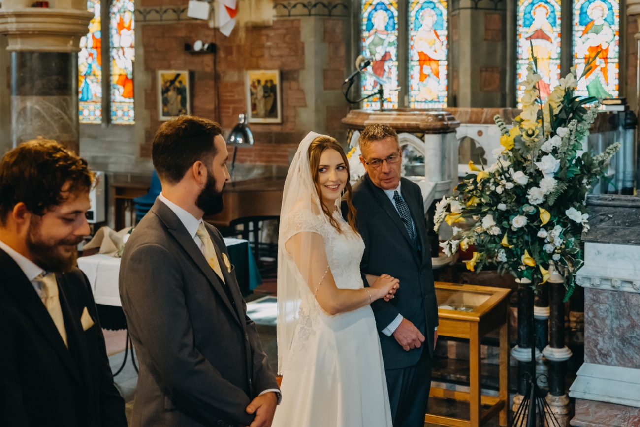 Bride smiles as her father gives her away during a heartfelt wedding ceremony at All Saints Church Babbacombe.