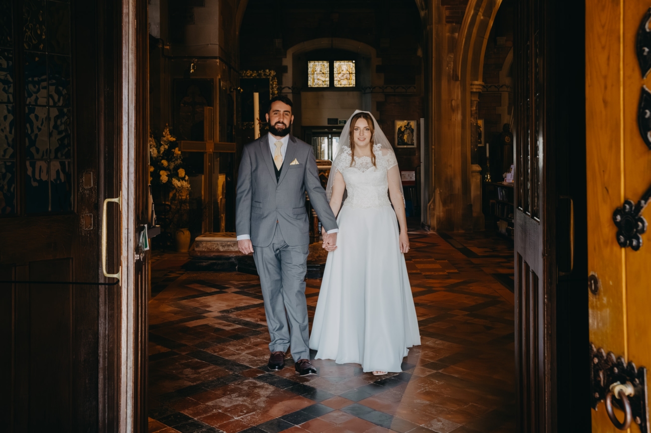 Newlyweds walk hand in hand through the doors of All Saints Church Babbacombe after their wedding ceremony.
