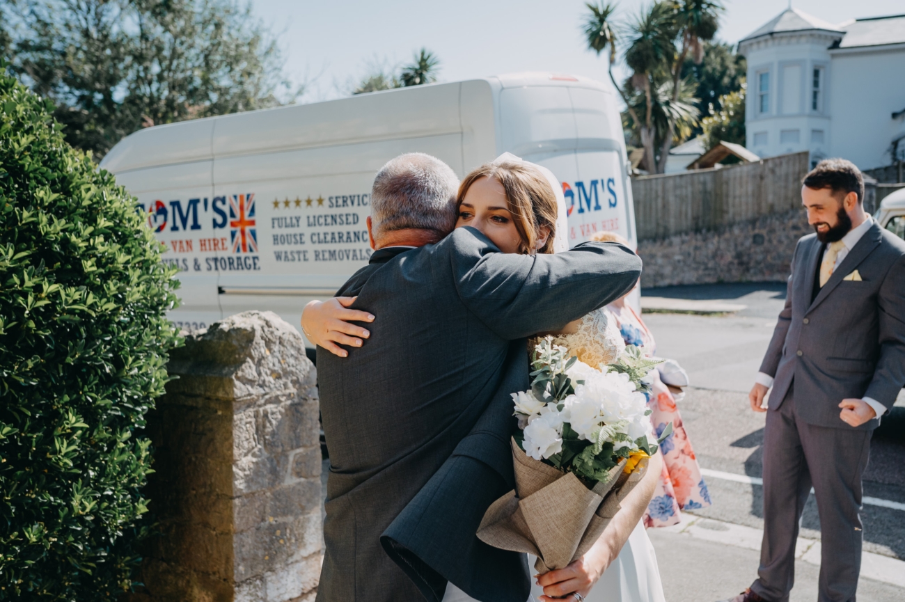 Candid moment as the bride shares a heartfelt hug outside All Saints Church Babbacombe.