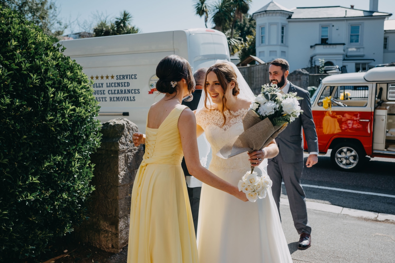 Bride sharing a joyful moment with her bridesmaid outside All Saints Church Babbacombe.