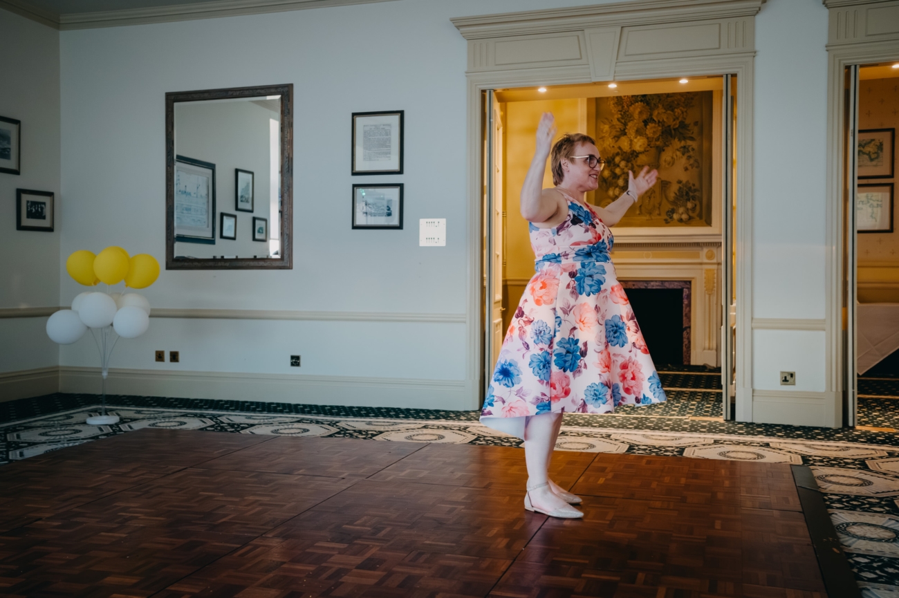 Person dancing joyfully in floral dress indoors.