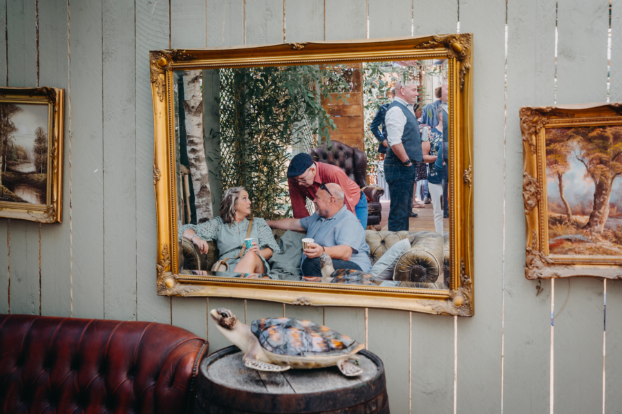 Wedding guests chatting on vintage sofa seen through mirror frame