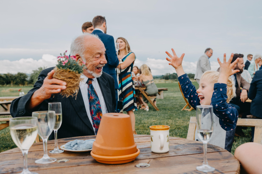 Grandfather laughing with grandson during outdoor wedding reception – candid guest photo