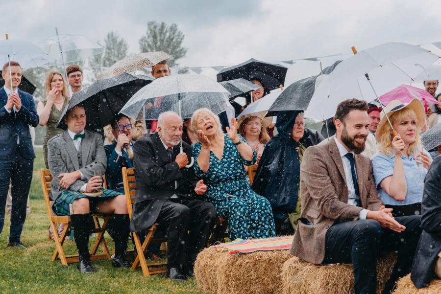 Wedding guests enjoying outdoor ceremony in the rain – natural reactions and umbrellas
