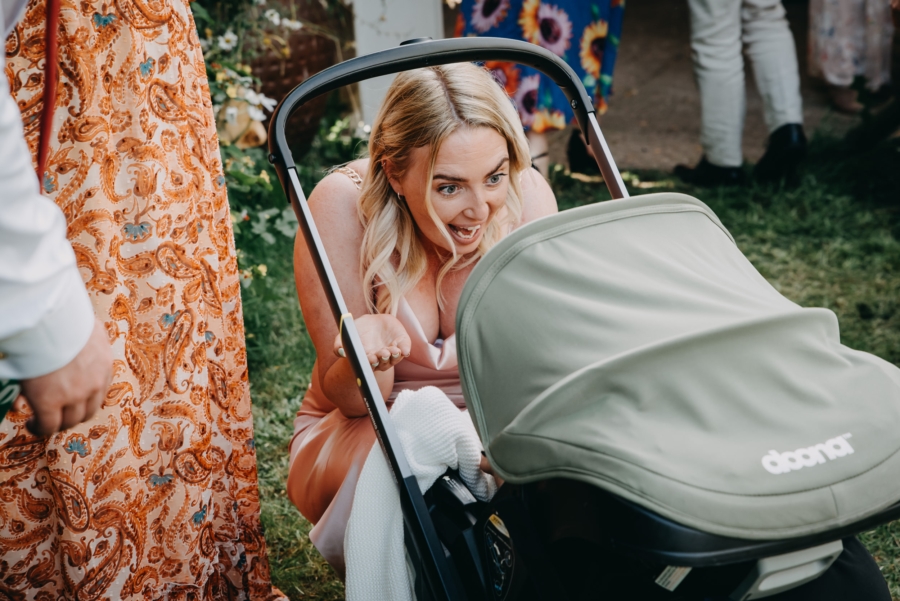 Wedding guest reacting joyfully to a baby in a pram, captured in a candid, unposed moment