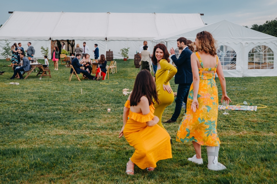 Three wedding guests dancing barefoot on the grass during a relaxed wedding celebration, captured naturally without direction