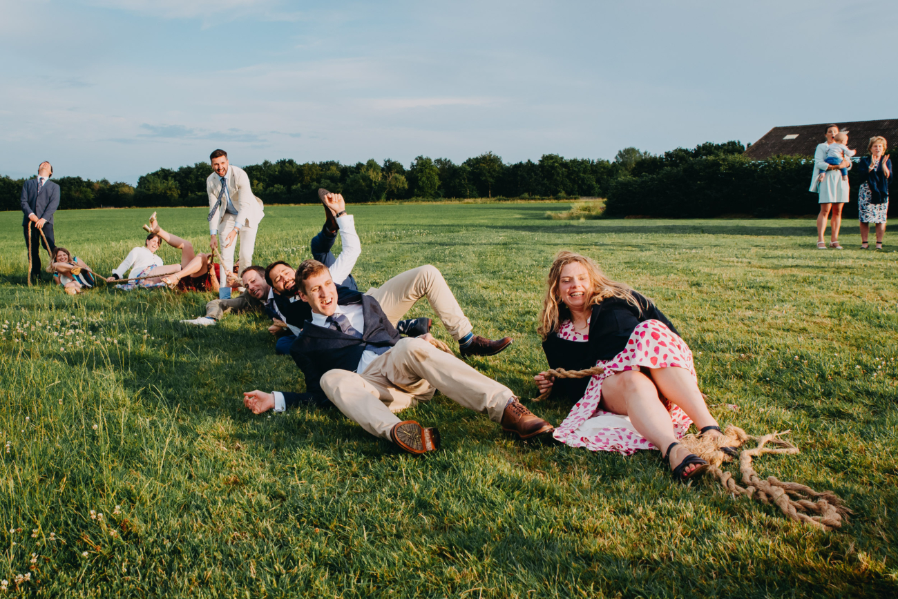Candid wedding guest photo of guests collapsing during tug of war – real wedding lawn games fun