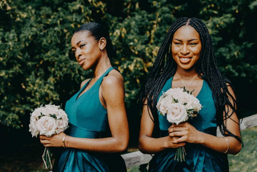 Bridesmaids in deep green-blue dresses holding pale rose bouquets