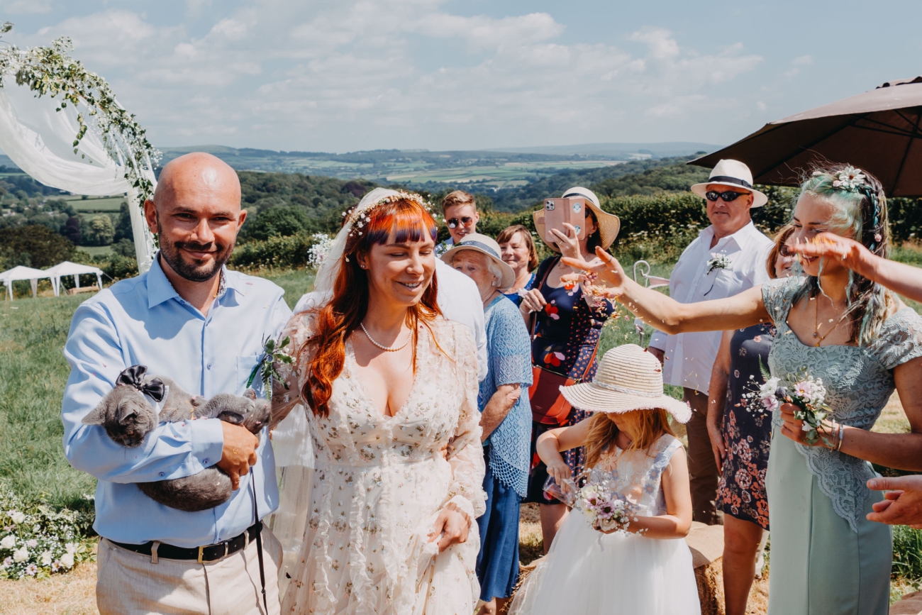 Bride and groom walking through confetti after outdoor wedding ceremony with guests celebrating