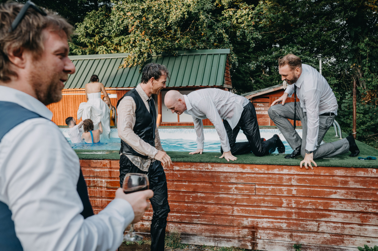 Soaked wedding guests helping each other out of the pool after a wild jump — documented by a candid wedding photographer in South Wales.