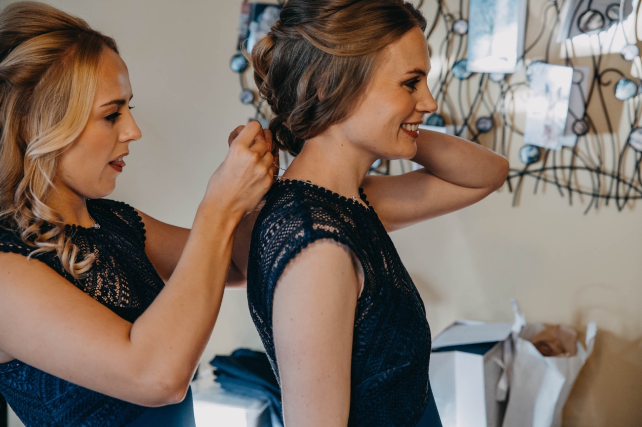 Bridesmaid fastening necklace before wedding ceremony in Myddfai – candid wedding photography moment