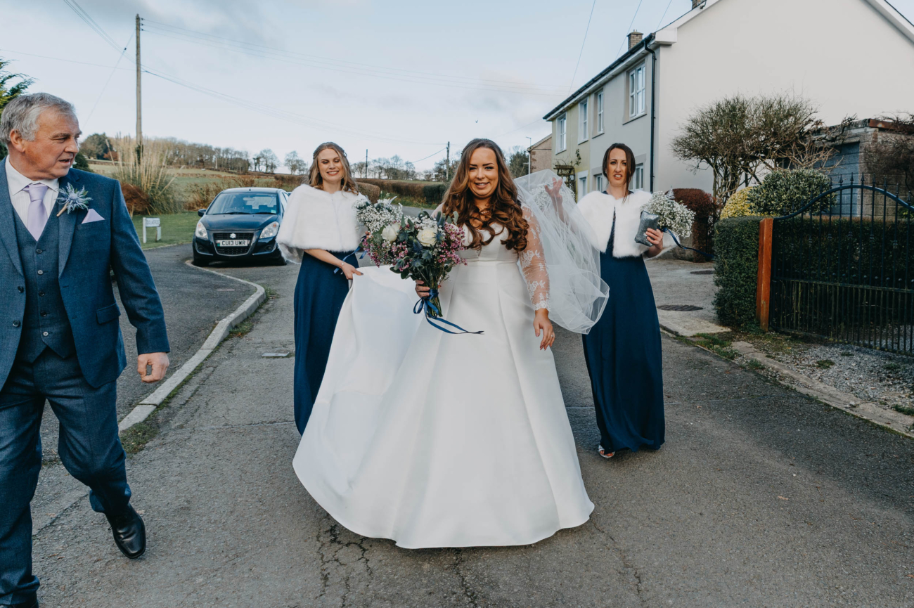 Bride walking through the village of Myddfai with her father and bridesmaids before the wedding ceremony