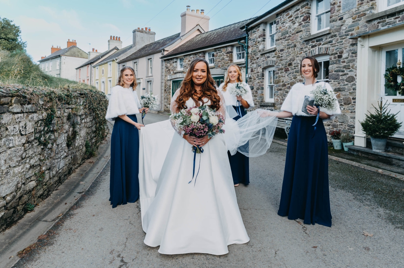 Bride and bridesmaids posing together on the village street before a winter wedding in Myddfai