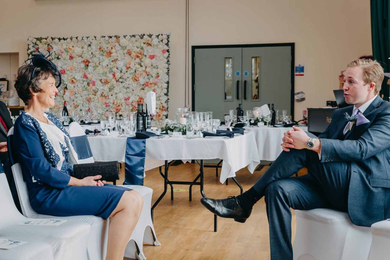 Relaxed conversation between groom and mother of the bride inside Myddfai Community Hall during the wedding day