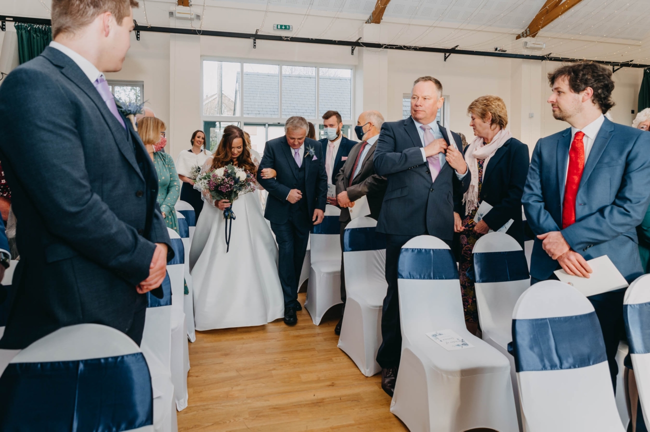 Bride walking down the aisle with her father at Myddfai Community Hall, surrounded by guests