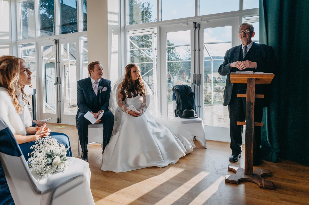 Bride and groom seated during their wedding ceremony at Myddfai Community Hall, listening to the celebrant