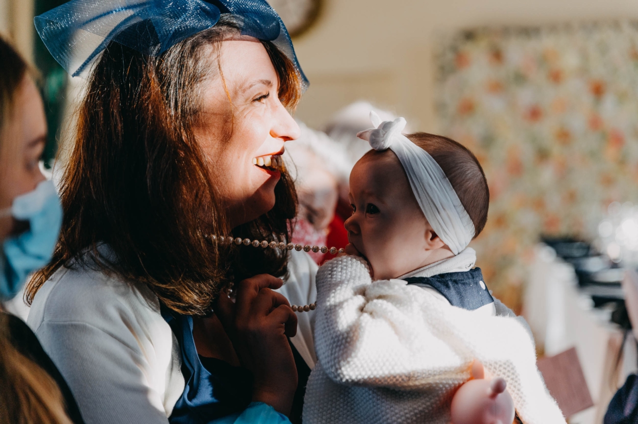 Wedding guest laughing while a baby plays with her necklace – candid moment during a Myddfai wedding celebration